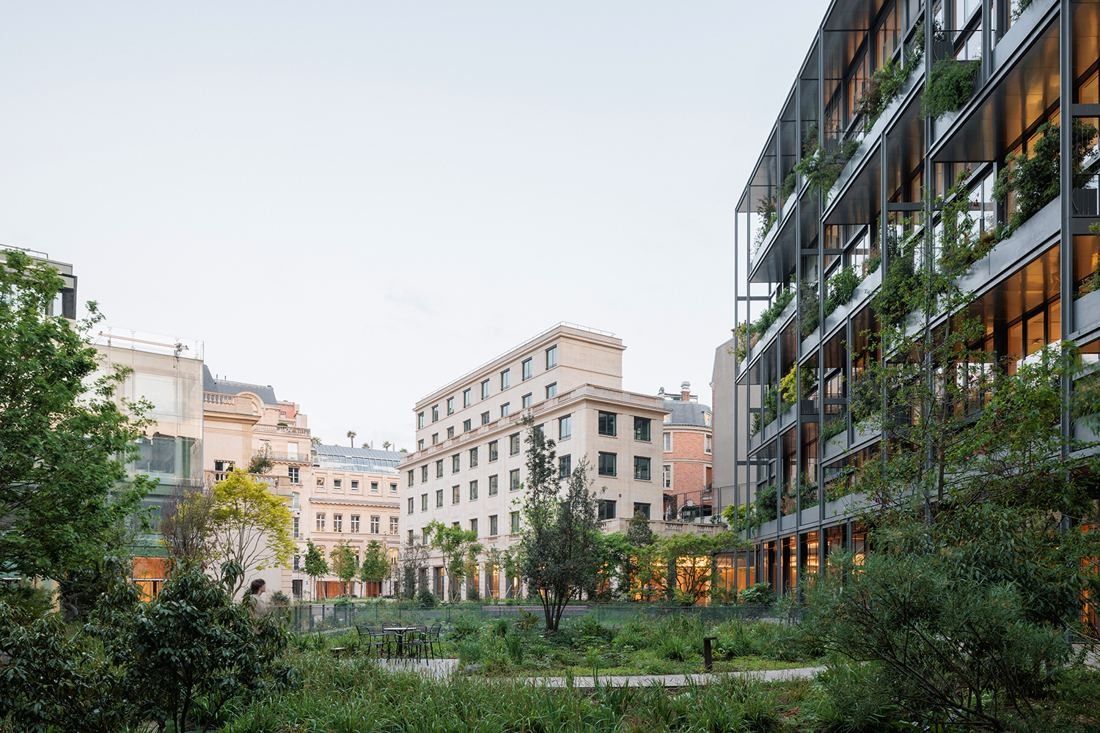 AXA: Wild-looking garden with stone buildings behind and a planted façade on the right