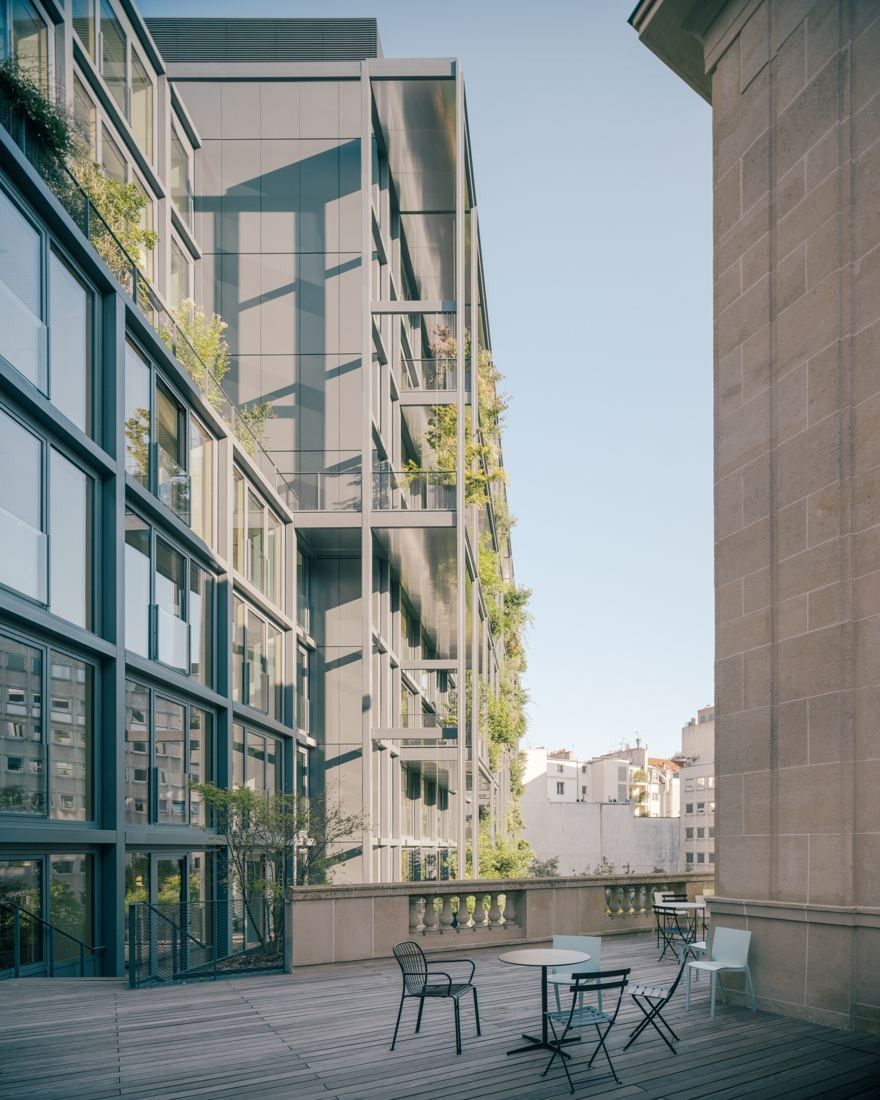 AXA: Wooden terrace with a table and chairs beside a planted façade and stone wall