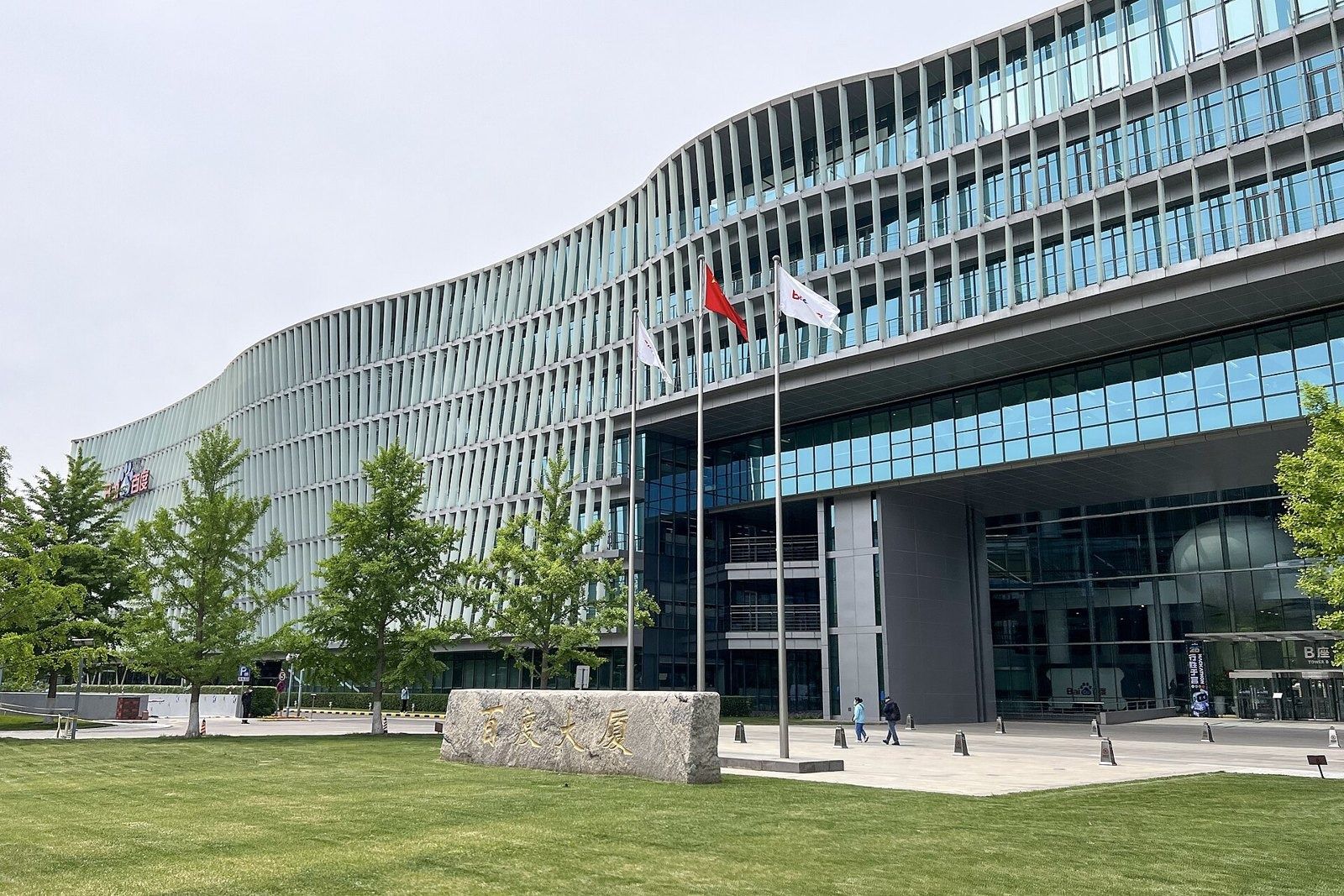 Baidu: Glass headquarters building with flagpoles and a stone marker in front