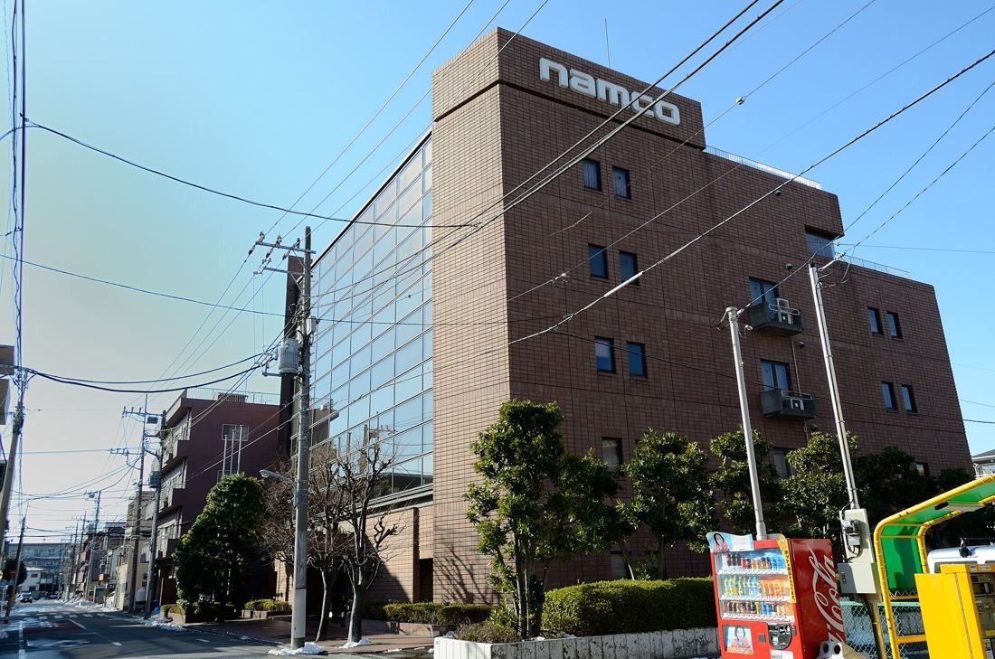 Brown brick-clad office building with a namco sign on the roof, beside a narrow street
