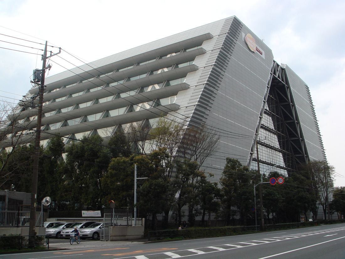 Large stepped office building with terraced floors behind a row of trees on a wide road