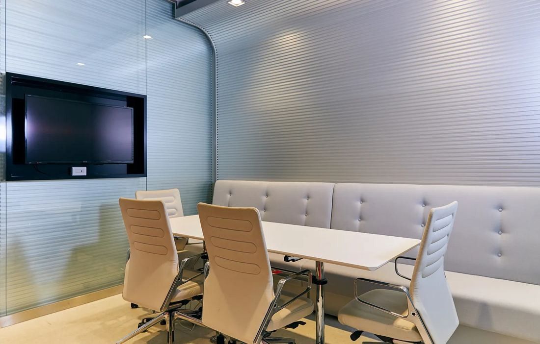 Bandai Namco: Meeting room with a quilted grey bench, white table, high-back chairs and a wall screen