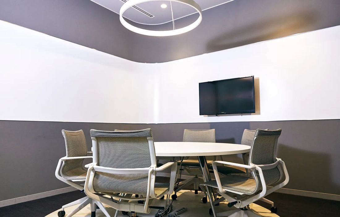 Bandai Namco: Round table with mesh chairs under a ring light in a white and grey meeting room