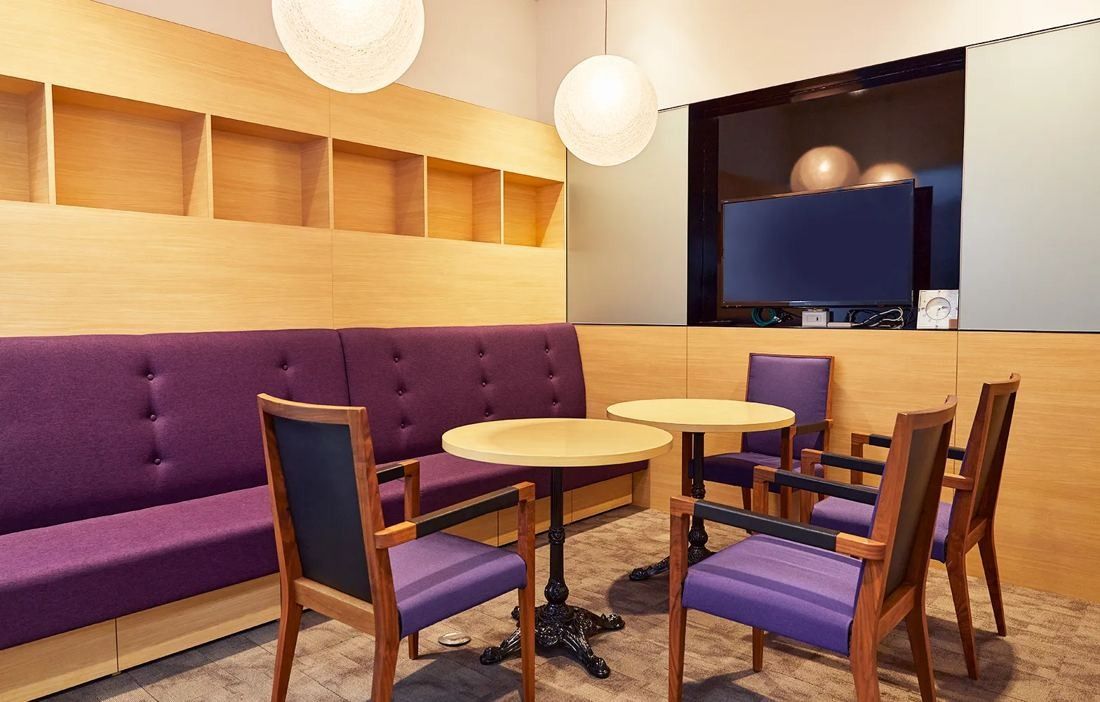 Bandai Namco: Small meeting space with a purple banquette, round tables and wooden chairs under globe lamps