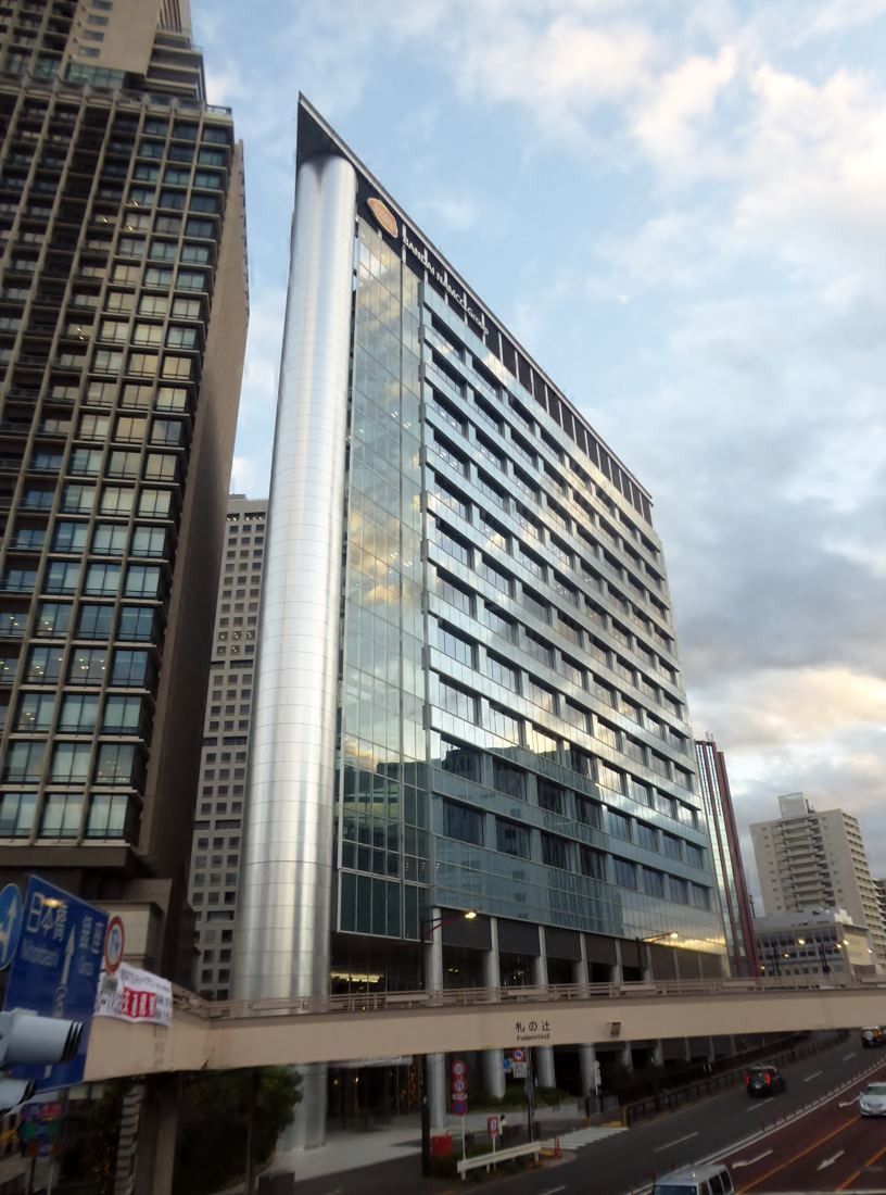 Bandai Namco: Tall glass and pale-panel office tower seen from street level against an evening sky