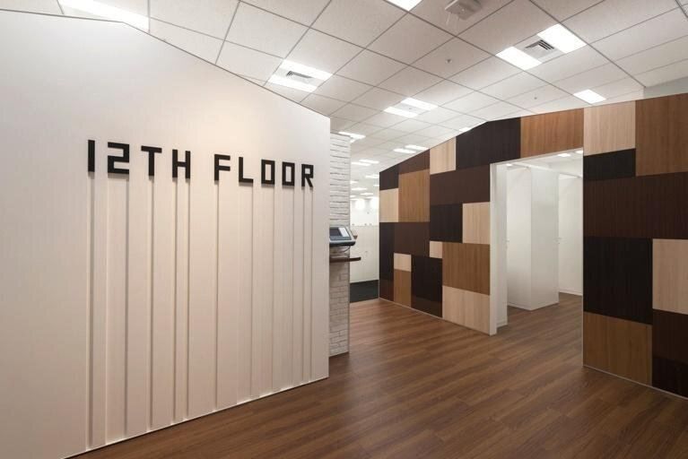 Bandai Namco: White wall lettered 12TH FLOOR beside a wall of wooden blocks in mixed shades