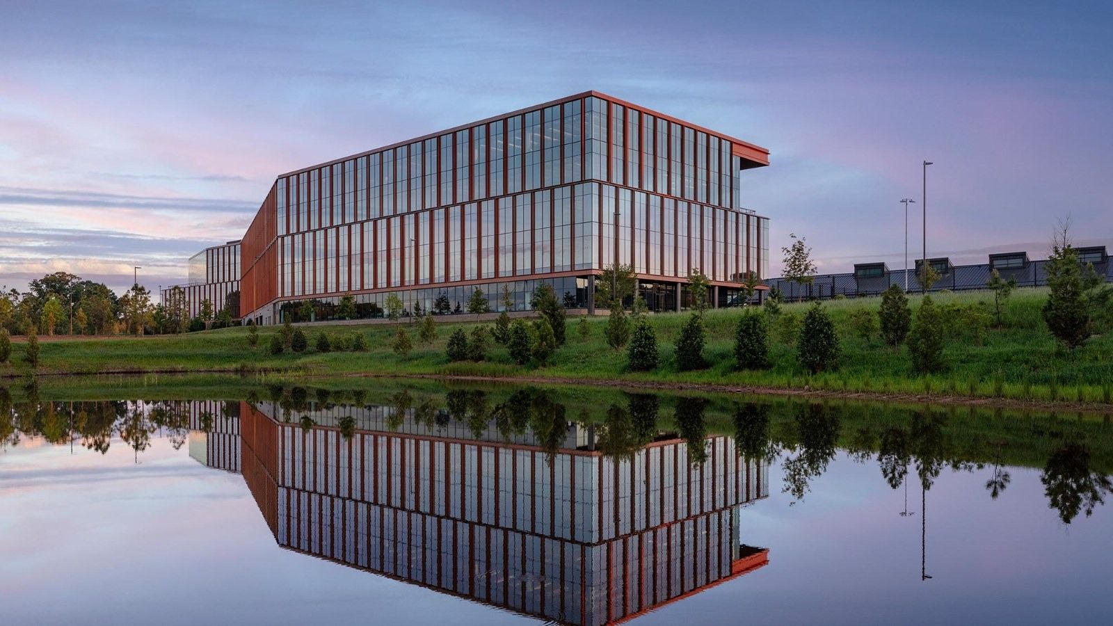 A long four-storey building reflected in a pond at dusk