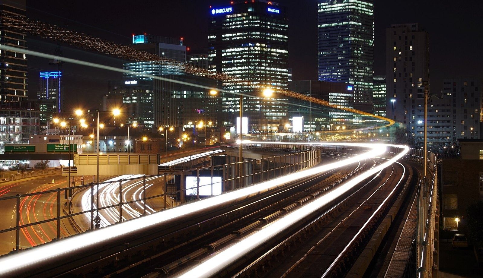 Barclays: Light trails of trains curving toward lit office towers at night