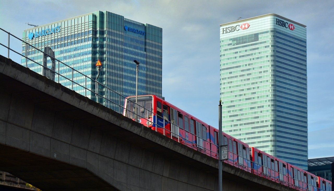 Barclays: Red light-rail train on a viaduct in front of two office towers