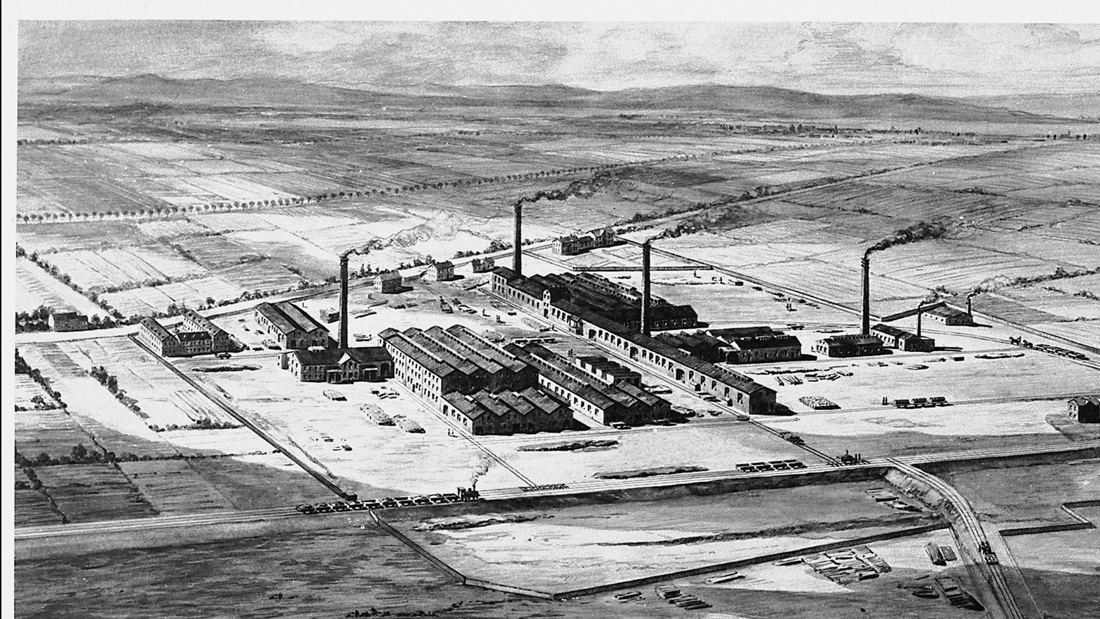 Black-and-white aerial view of an early factory with chimneys on flat land