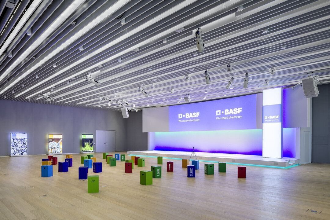 Conference hall with a lit stage, wooden floor and colourful cube seats