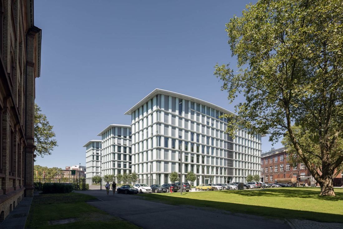 Long white-and-glass office block beside a lawn and a large tree