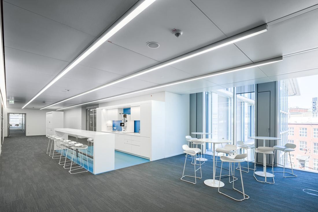 Open area with a white counter, bar stools and high tables by the windows