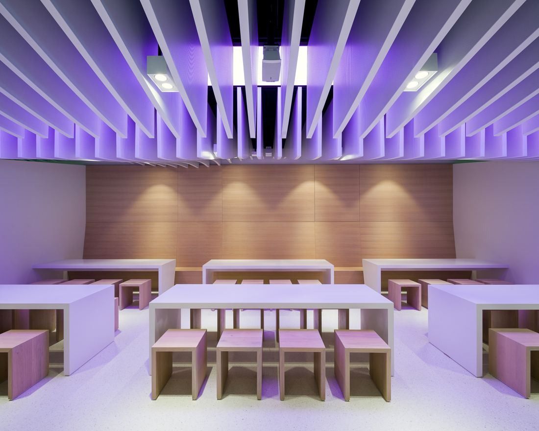Seating area with wooden stools and tables under purple-lit ceiling slats