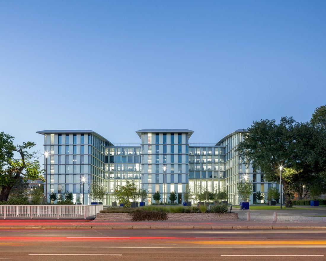 Symmetrical glass facade of an office building seen across a road with light trails at dusk