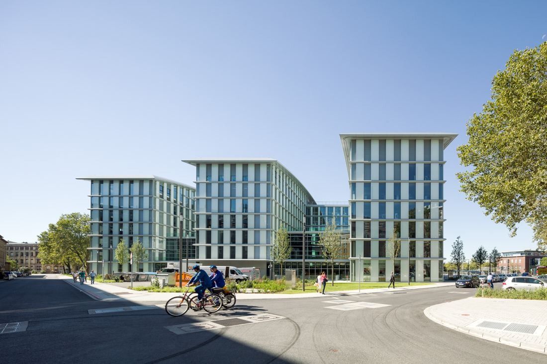 Three glass office blocks of different heights with cyclists passing in front
