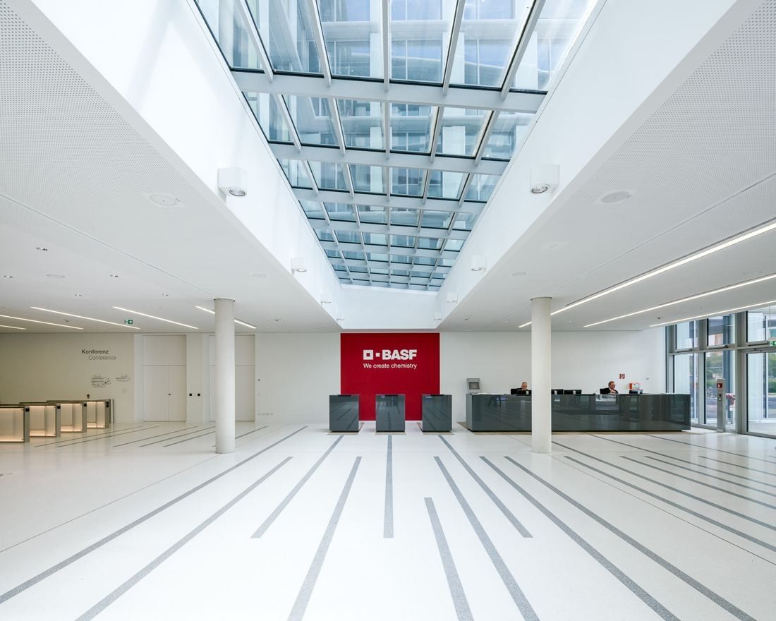 White entrance hall under a glass roof with a red reception wall at the far end