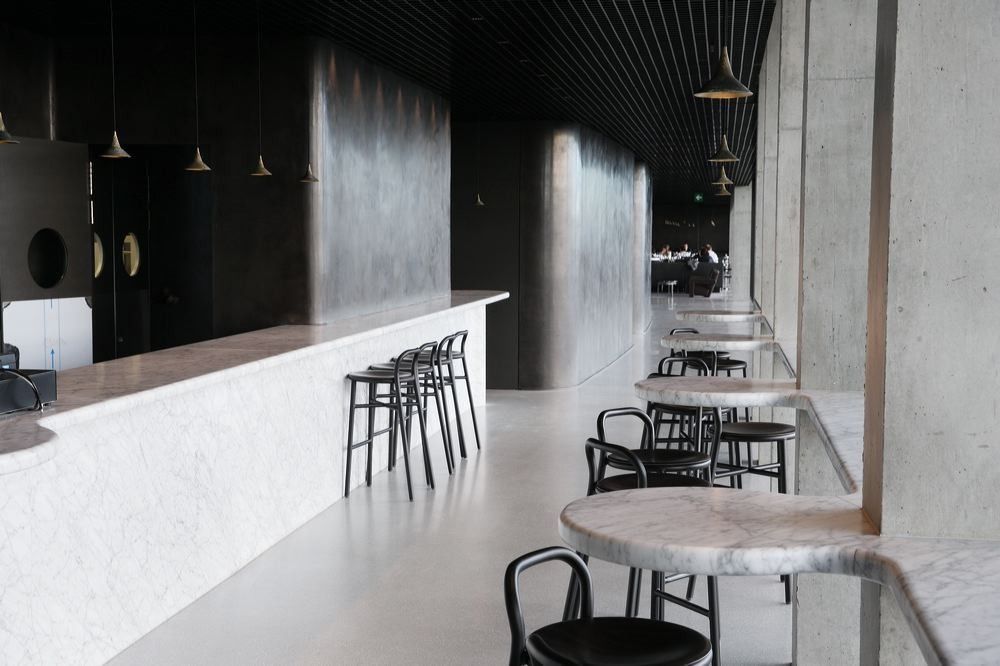 BBVA: Bar counter with stools and small round tables beside a concrete wall