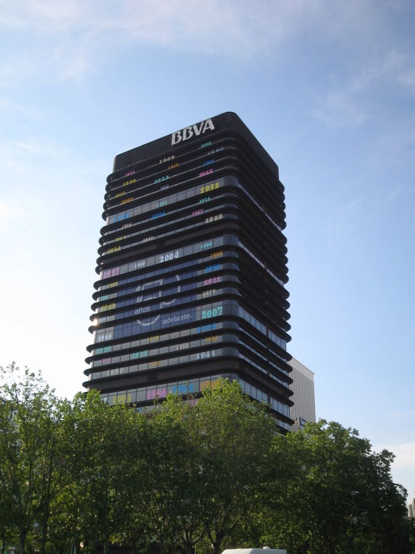 Dark banded office tower above trees under a blue sky