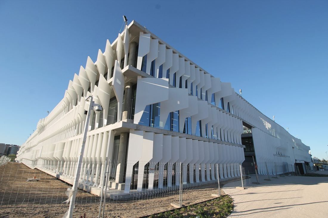 BBVA: Long low-rise building wrapped in sculpted white vertical fins under a blue sky