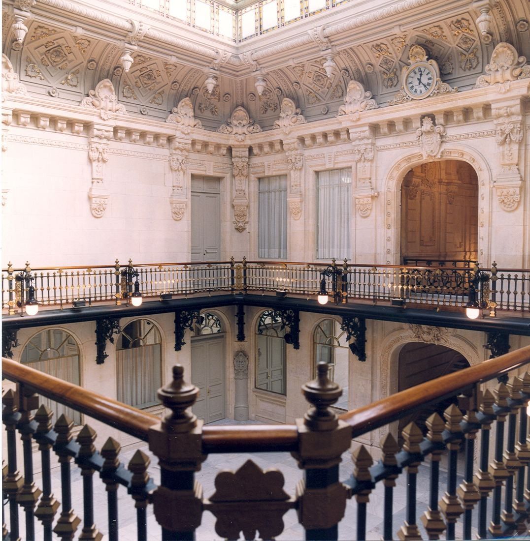 Ornate interior with a wrought-iron balcony railing around a stairwell under a skylight