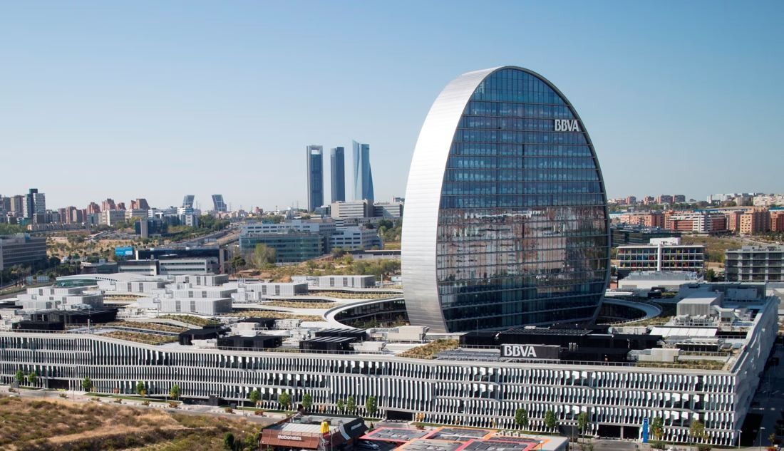 BBVA: Oval glass tower above a low-rise complex with green roofs, with skyscrapers on the horizon
