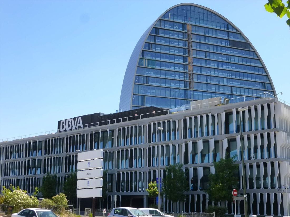 BBVA: Oval tower behind a low-rise building with white vertical fins and a garden in front