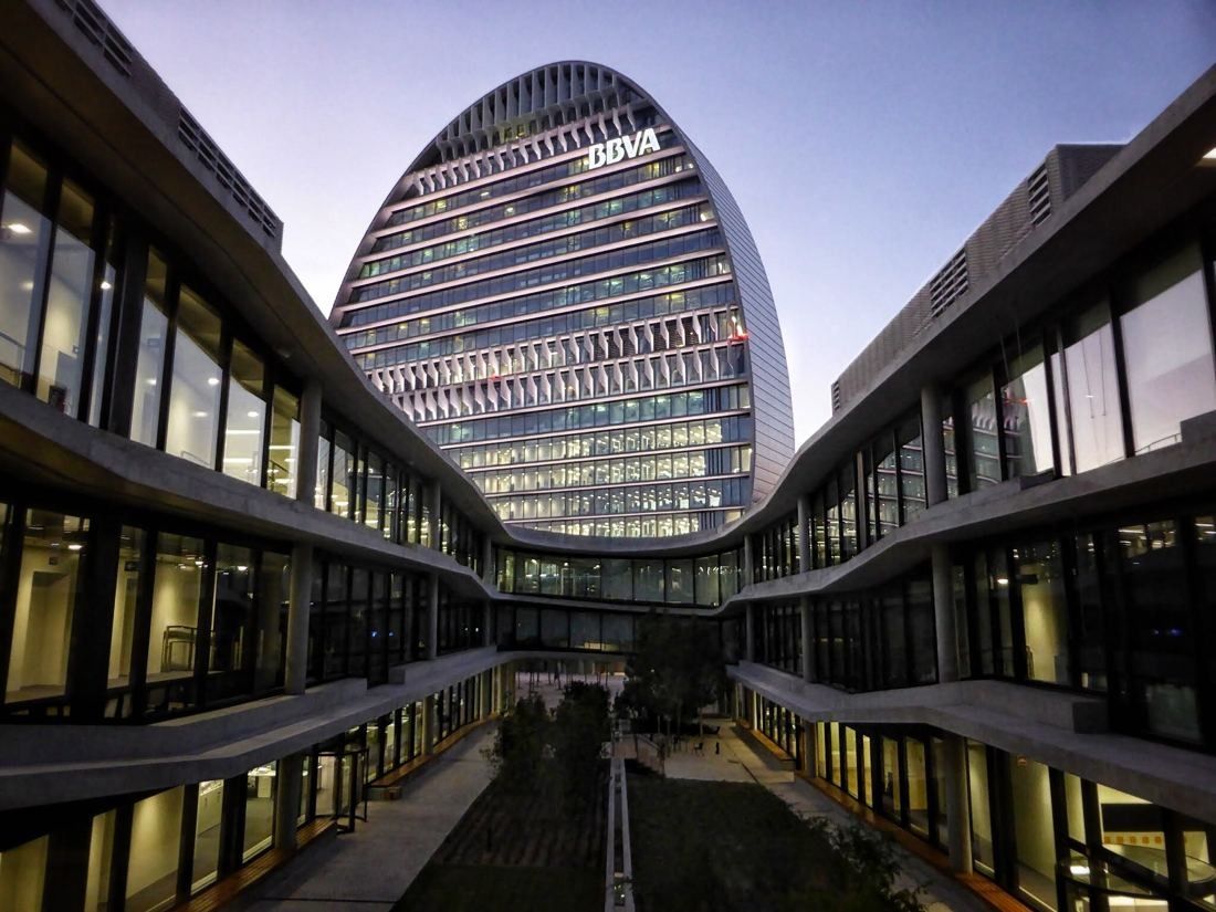 BBVA: Oval tower seen down a long courtyard between glazed office wings at dusk
