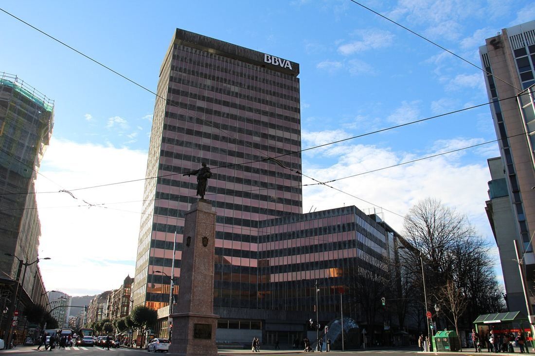 Tall office tower and lower building at a street corner with a statue on a column
