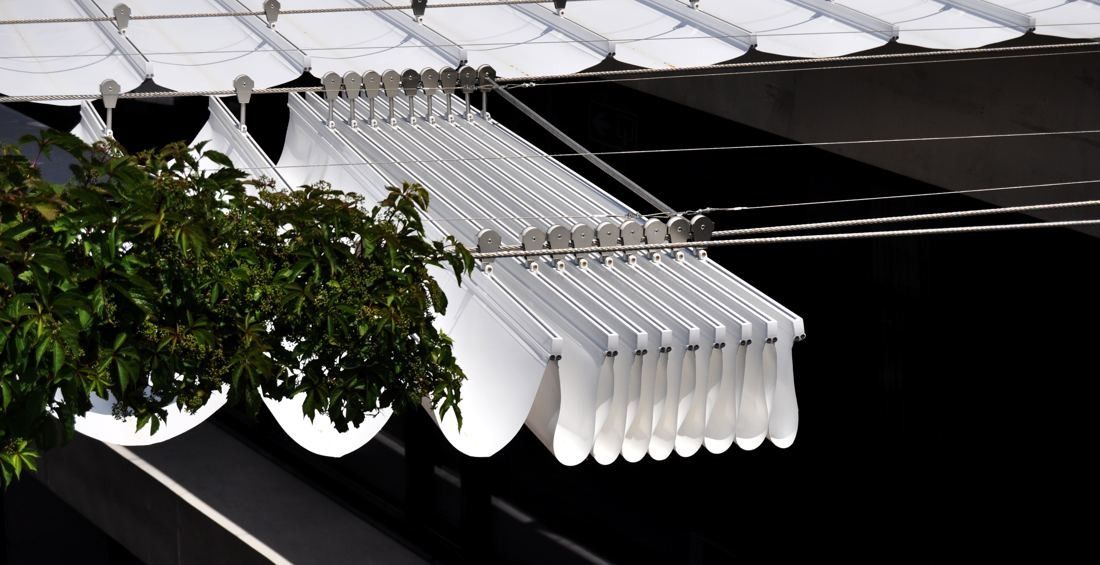 BBVA: White fabric awnings stretched over a lane next to tree leaves