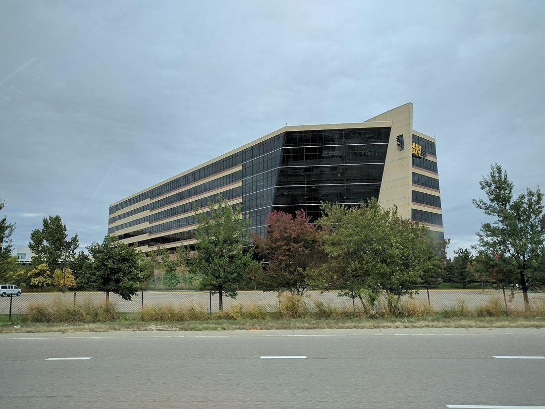 Best Buy: Angular glass office tower with horizontal bands seen from a road lined with trees