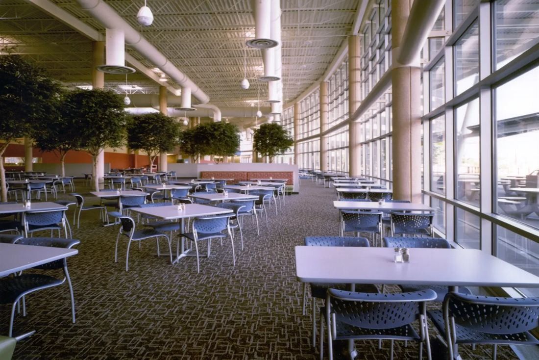 Best Buy: Long dining area with tables and chairs beside a full-height glass wall and indoor trees