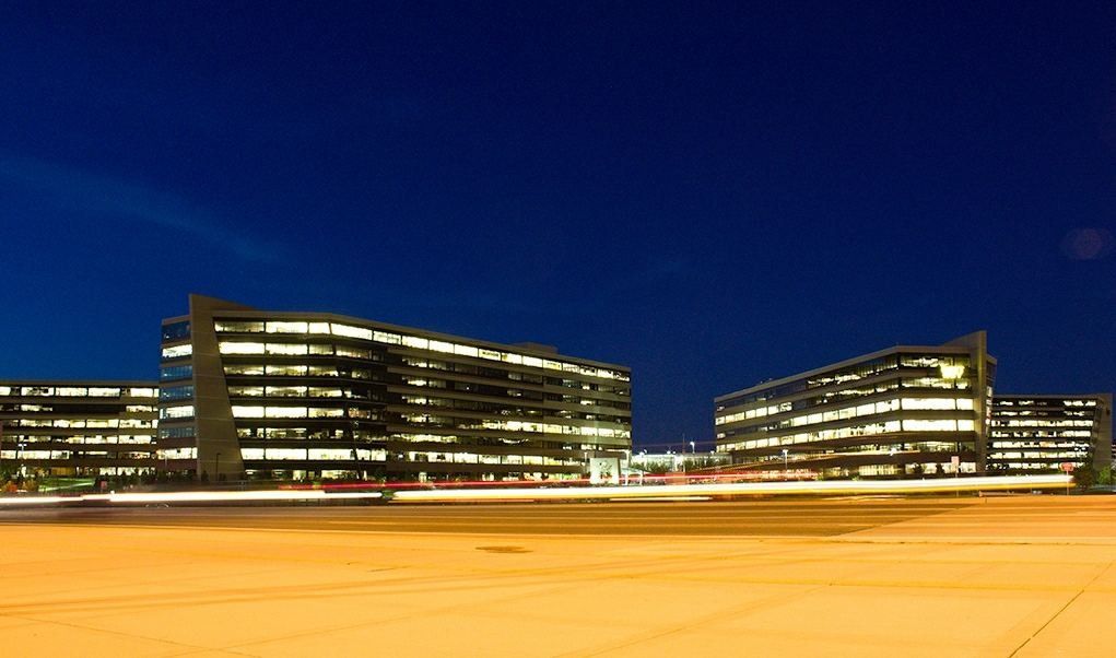 Best Buy: Office towers with lit windows against a deep blue night sky, light trails on the road in front