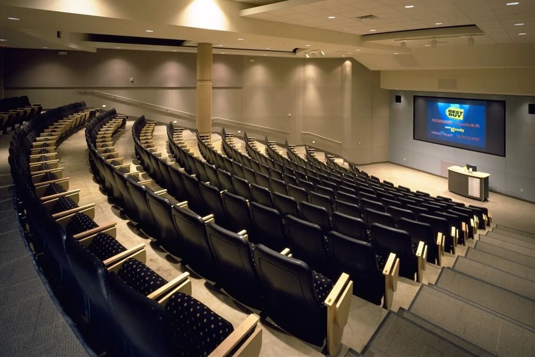 Best Buy: Tiered auditorium with rows of dark seats facing a large screen