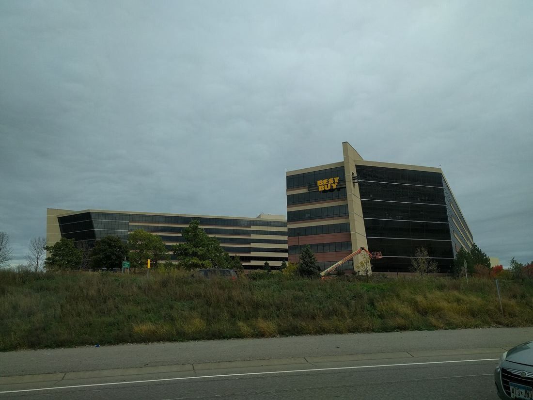 Best Buy: Two office buildings with angled ends seen over a grassy slope under a grey sky