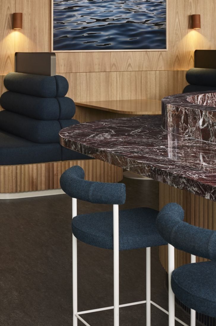 BHP: Blue curved stools at a dark marble counter below an ocean artwork