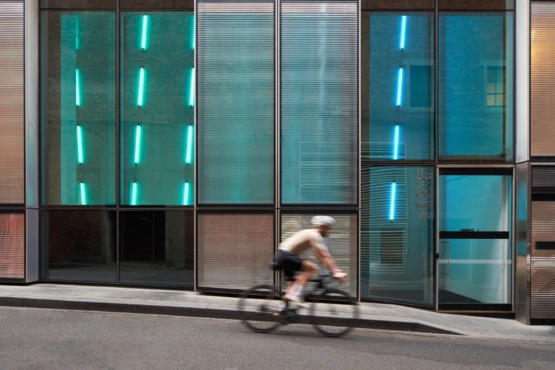 BHP: Cyclist riding past a glass street-level facade lit with teal light