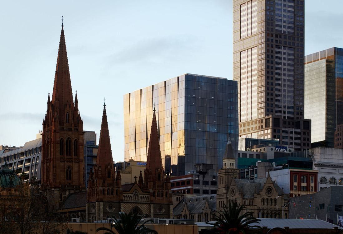 Dark glass office tower rising behind the Gothic spires of a stone cathedral at dusk