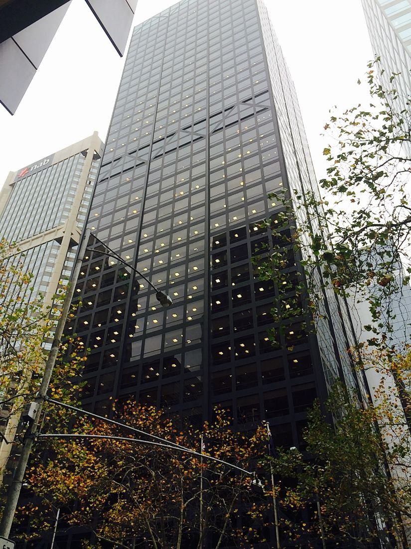 Dark steel and glass skyscraper seen from the street among trees