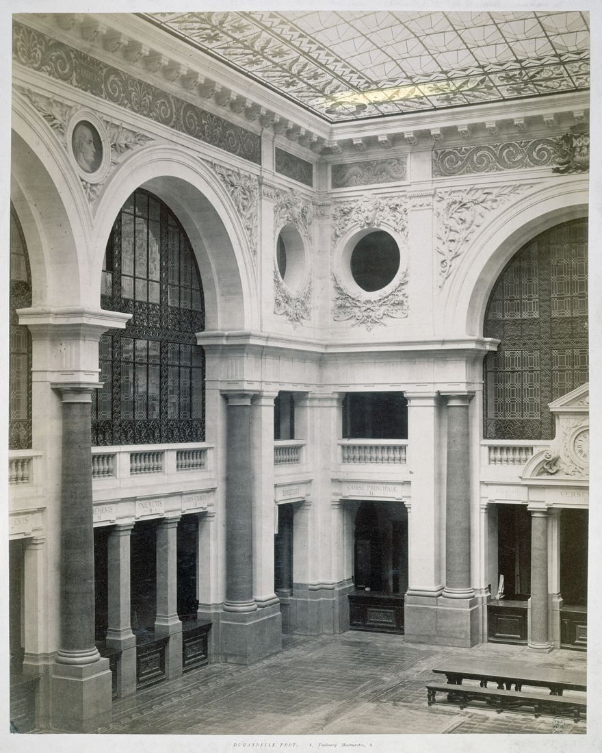 Black-and-white photo of a stone courtyard with large arched windows and columns