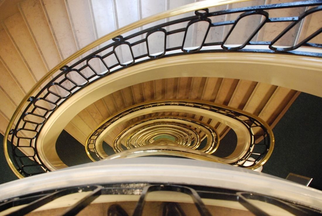 BNP Paribas: Looking up an oval spiral staircase with a dark metal balustrade and brass rail