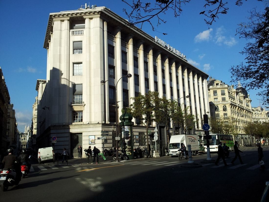 Pale stone Art Deco office building with tall pilasters and a BNP Paribas sign on a sunny boulevard corner