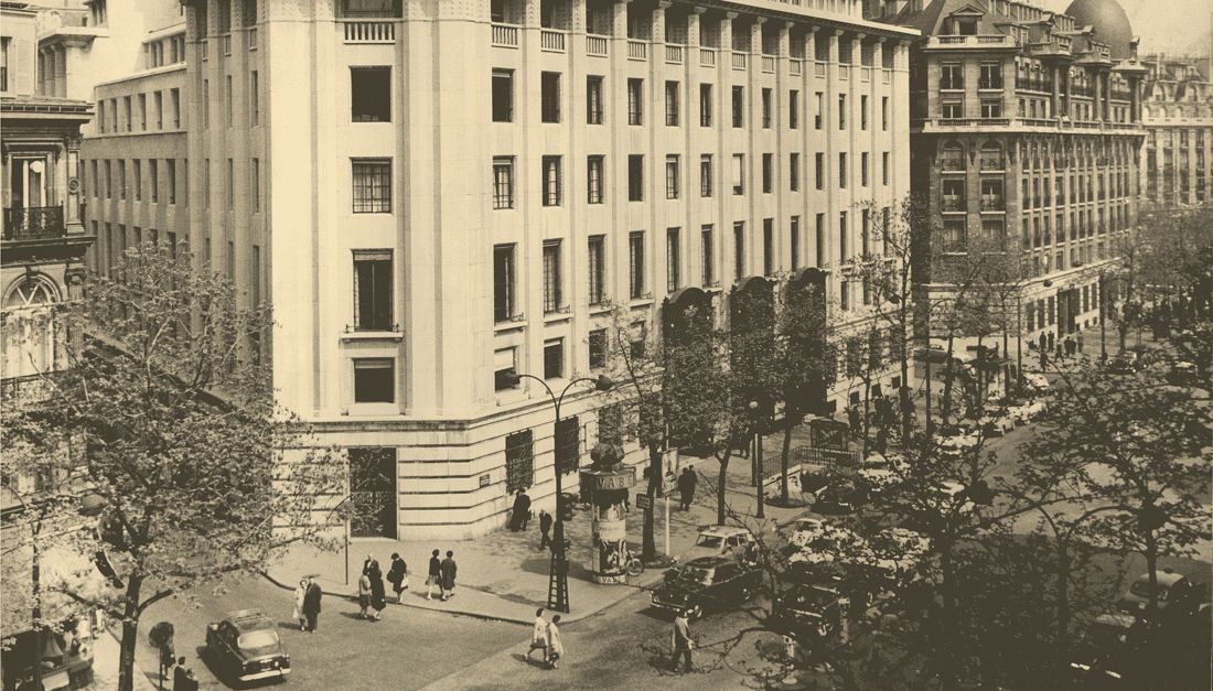 Sepia photo of the stepped stone building on a tree-lined boulevard corner