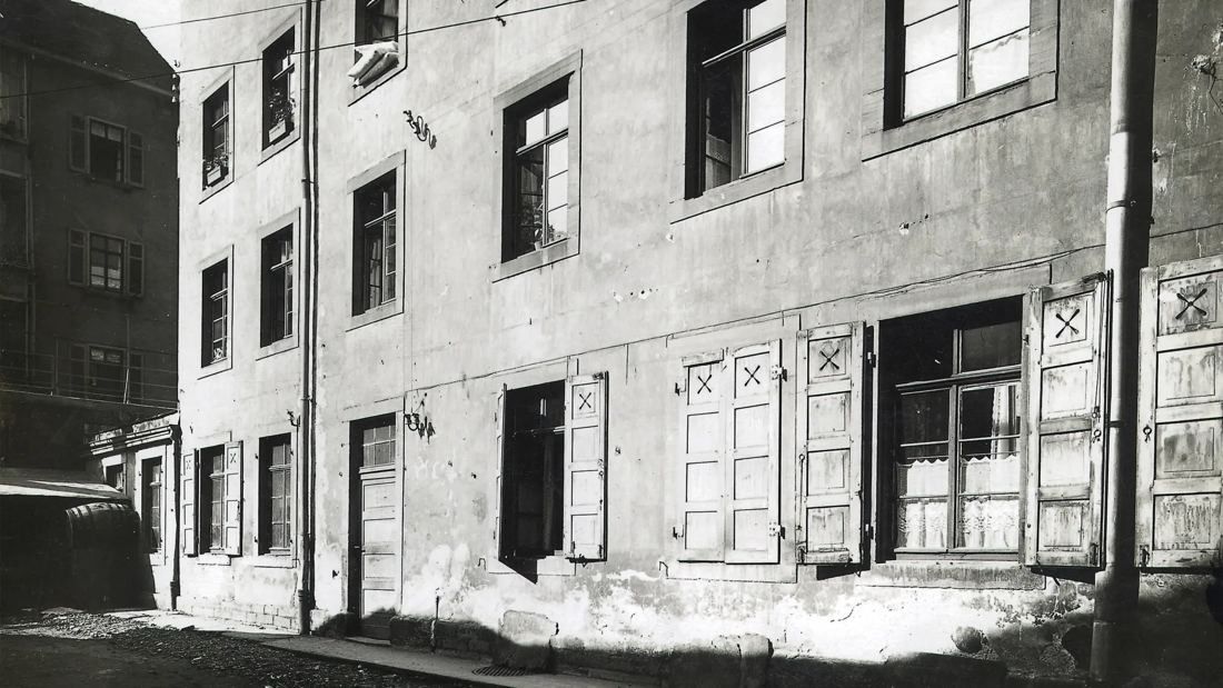 Black-and-white photo of the plain plastered rear façade of an old building with shuttered windows