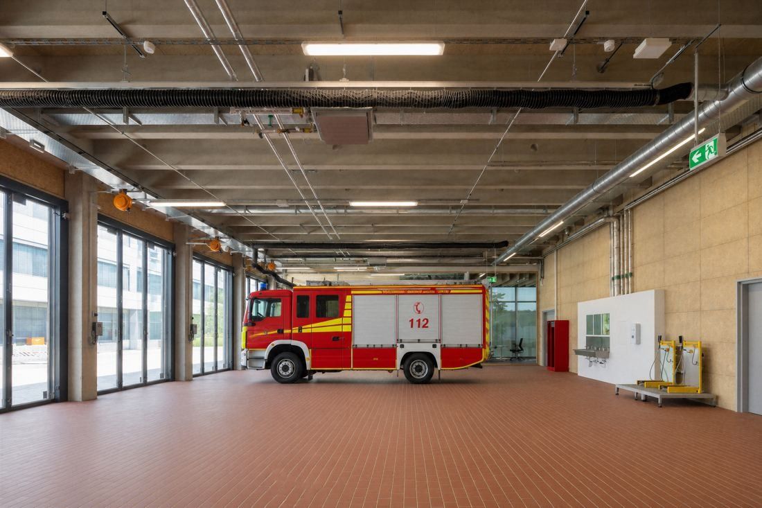 Bosch: Hall with terracotta floor, timber walls and a red fire engine parked by large glass doors