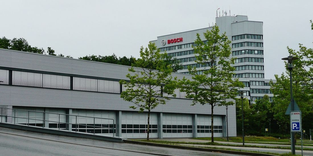 Bosch: Long low grey building with young trees in front and a white office tower behind
