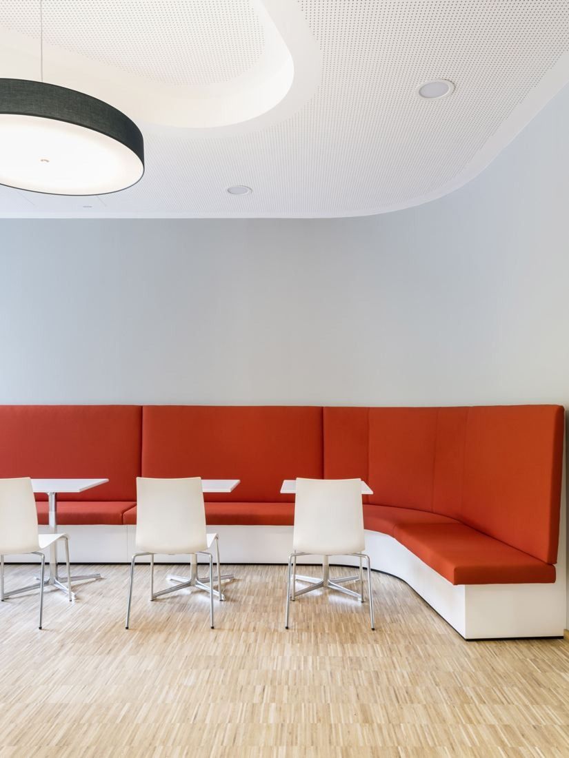 Bosch: Red upholstered bench seating along a wall with white chairs and tables