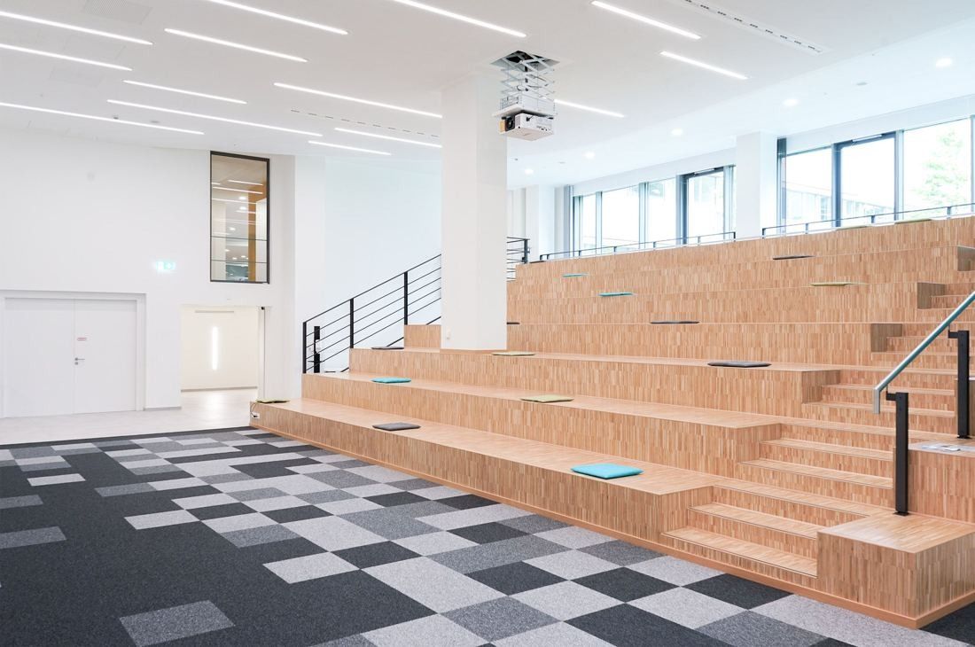 Bosch: Wide timber seating steps beside a staircase in a bright room with patterned carpet