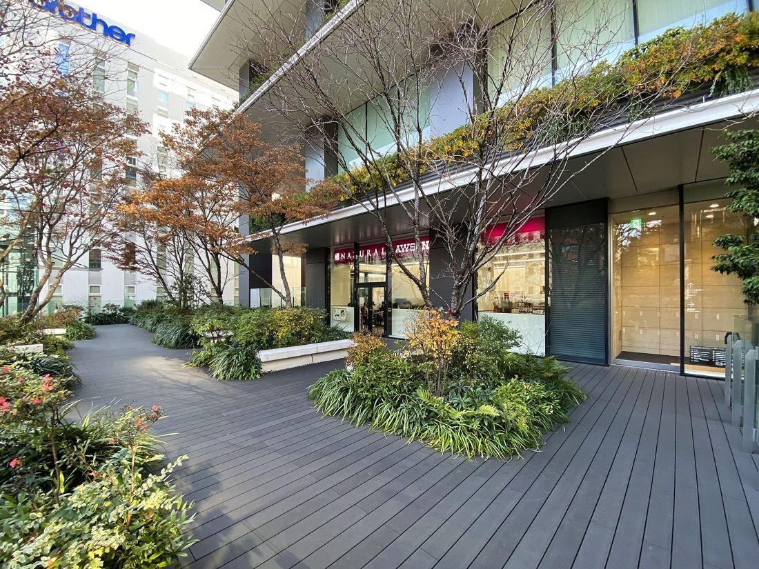 Bridgestone: A wooden deck path among shrubs and trees beside the building's glass facade