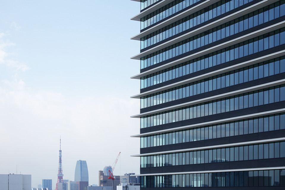 Bridgestone: The banded glass facade of the tower against the sky, with Tokyo Tower in the distance